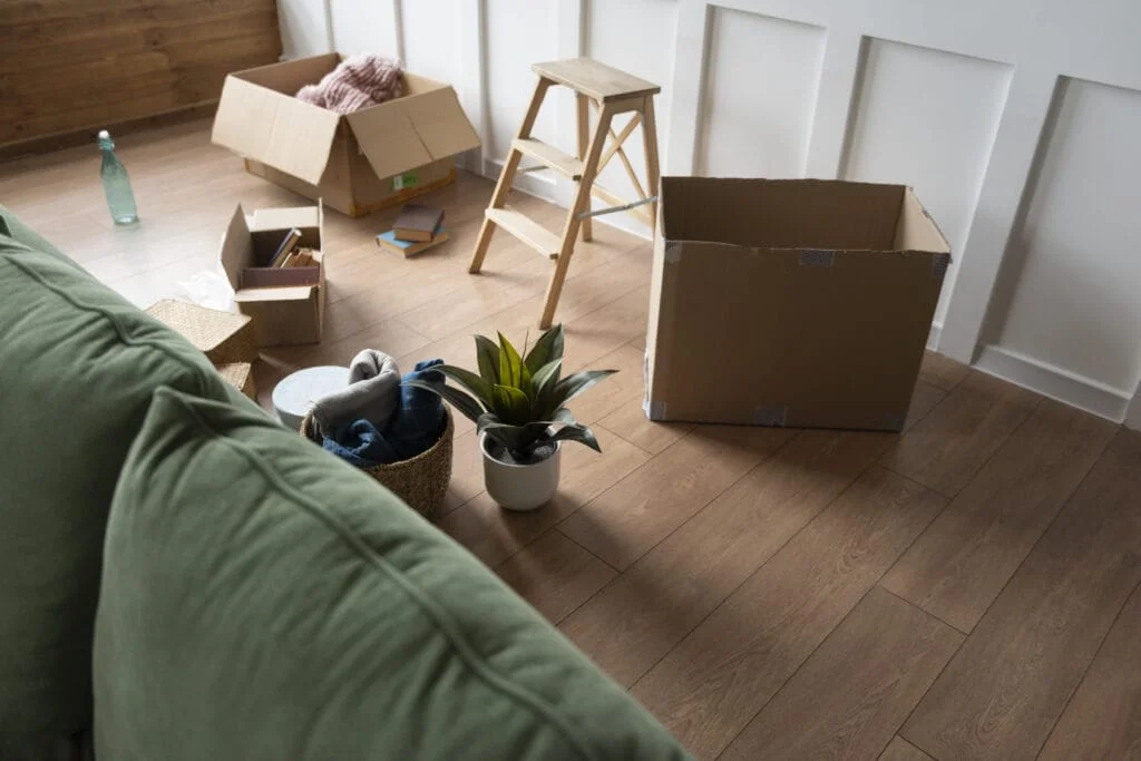 Unpacking or packing process with open cardboard boxes and household items on a wooden floor, ready for move out cleaning.